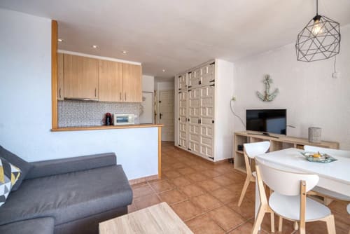 Modern apartment kitchen-living area in Palafrugell with wooden cabinets, dining table, TV, and sea view terrace access