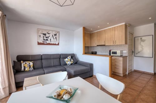 Modern apartment living room with kitchen at Finques Garcia Enrich, Palafrugell. Gray sofa, dining table, wood cabinets.