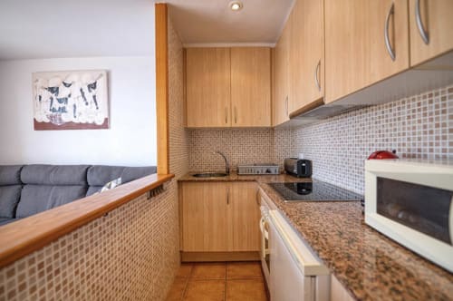 Modern kitchen with wooden cabinets, granite countertops, and mosaic tile backsplash in Palafrugell apartment with sea views