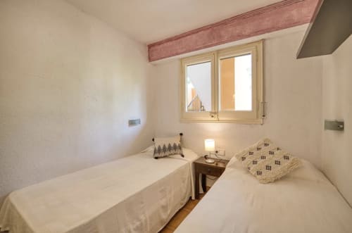 Cozy twin bedroom in Palafrugell apartment with sea views, two single beds, wooden beam, and window overlooking building