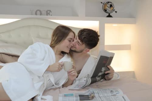 Coppia che si rilassa a letto presso l'Enjoy House Bracciano con caffè e giornale, camera moderna con decorazioni a globo