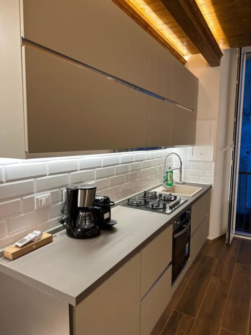 Cucina moderna nell'appartamento Enjoy House Bracciano con piastrelle bianche, piano cottura a gas e travi in legno a vista