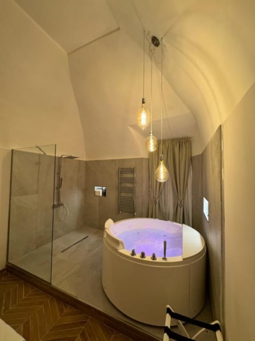 Lussuoso bagno moderno presso l'Enjoy House Bracciano con vasca idromassaggio illuminata, doccia a pioggia e illuminazione a sospensione a Bracciano