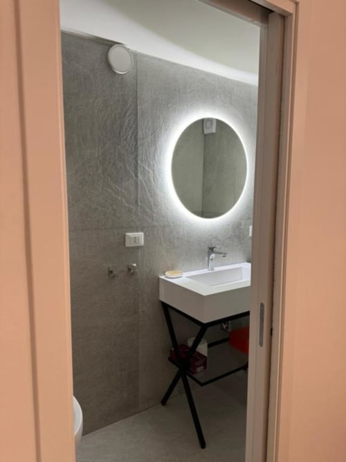 Bagno moderno presso Enjoy House Bracciano con specchio rotondo illuminato, lavabo bianco e mobile sottolavabo scuro