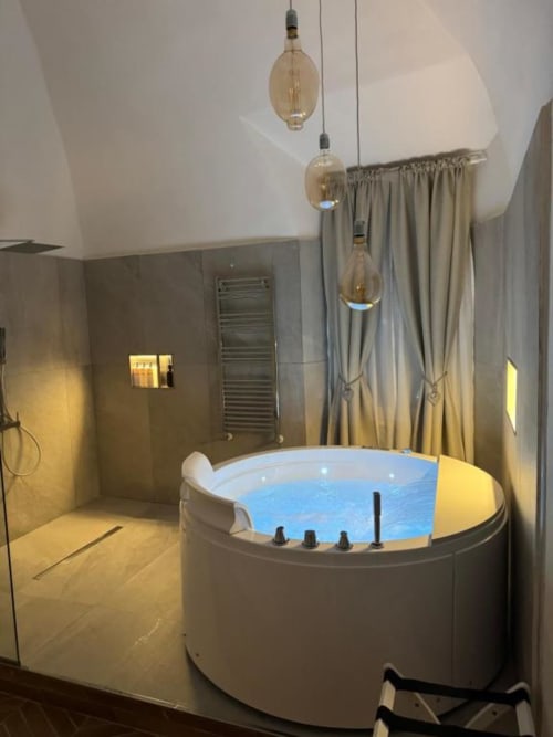 Bagno spa lussuoso a Enjoy House Bracciano con vasca idromassaggio rotonda illuminata, soffione a cascata e lampada sospesa