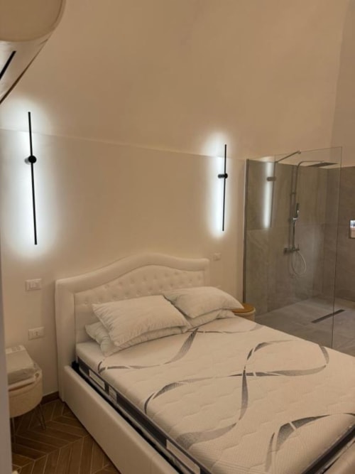 Camera da letto moderna con letto matrimoniale, luci lineari a parete e cabina doccia in vetro presso Enjoy House Bracciano