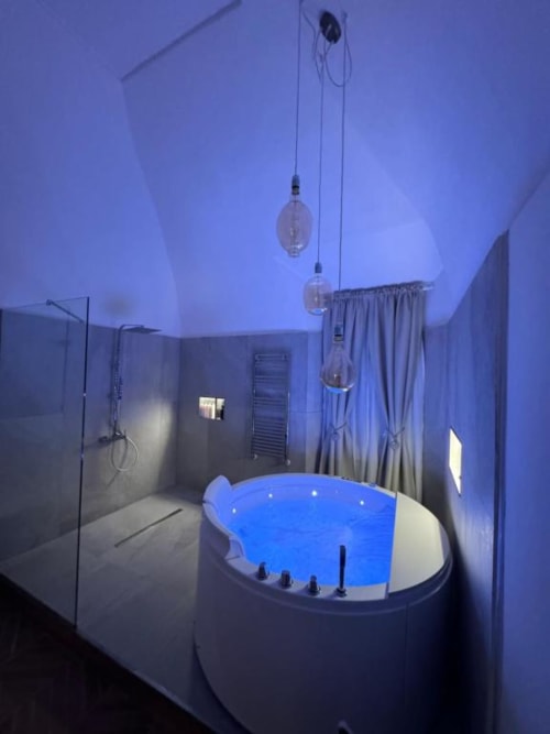 Moderno bagno con vasca idromassaggio illuminata in blu, doccia in vetro e luci a sospensione nell'appartamento Enjoy House Bracciano.