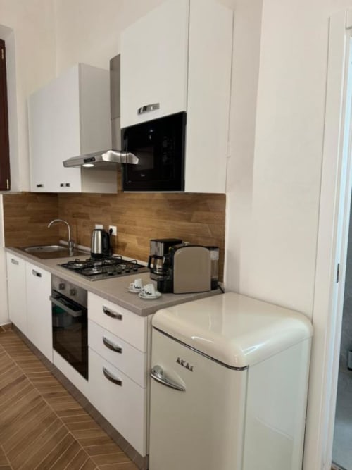 Moderna cucina bianca con piano cottura a gas, frigorifero color panna e rivestimento in legno nell'appartamento di Bracciano