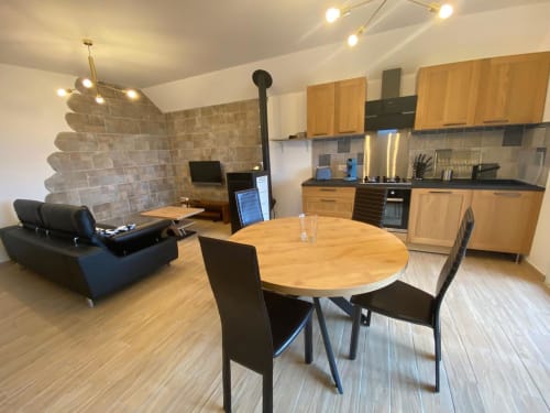 Intérieur ouvert du gîte avec table à manger en bois, cuisine, cheminée et canapé noir au Domaine du Bez