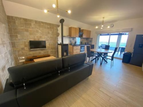 Séjour moderne avec canapé noir, poêle à bois, cuisine et vue sur les montagnes au Domaine du Bez, Saint