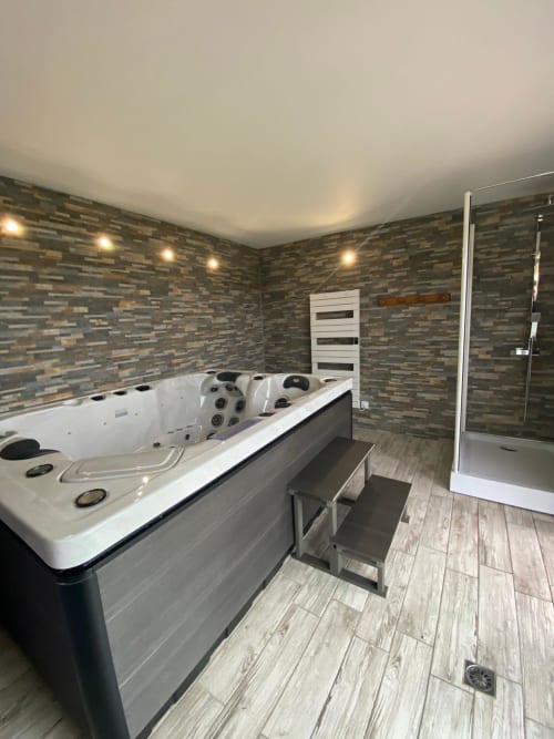 Salle de bain spa luxe avec baignoire jacuzzi, mur en pierre, douche à effet pluie et sèche-serviettes chauffant au gîte Le Domaine du Bez