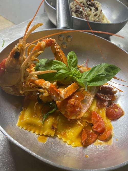 Raffinato piatto di ravioli di astice presso Enjoy House Bracciano, guarnito con basilico fresco e pomodori