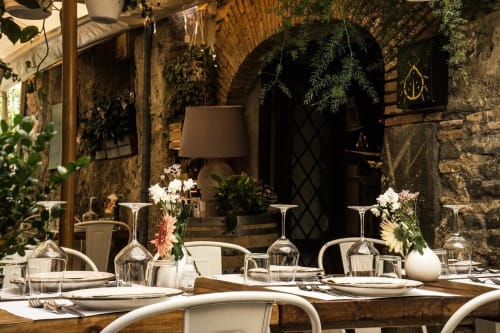 Elegante allestimento per cena esterna presso Enjoy House Bracciano con arco in pietra, suppellettili bianche, fiori freschi e atmosfera suggestiva