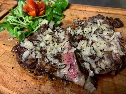 Bistecca affettata con burro alle erbe su tagliere di legno, fresca insalata e peperone rosso all'Enjoy House Bracciano