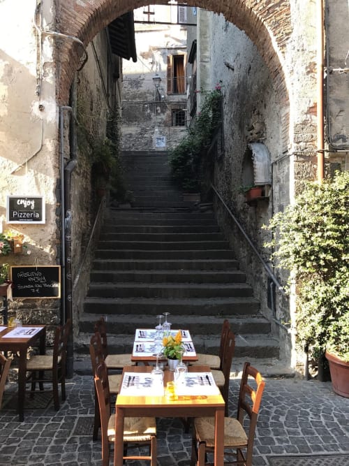 Area ristorazione all'aperto della pizzeria a Bracciano con tavoli sotto un'arcata in pietra medievale e scale