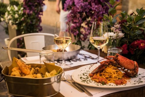 Elegante cena all'aperto presso Enjoy House Bracciano con vino bianco, aragosta alla griglia e patatine tra fiori viola