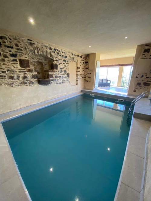Piscine intérieure du gîte Le Domaine du Bez à Saint Laurent d'Olt avec murs en pierre et vue sur les montagnes