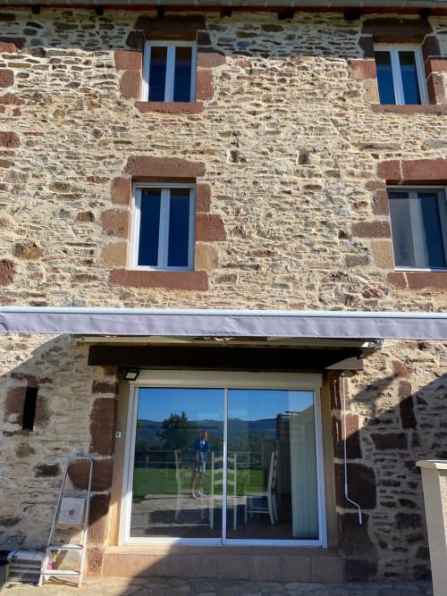 Façade de maison en pierre au Domaine du Bez avec fenêtres à cadre bleu et portes vitrées surplombant les montagnes, Saint Laurent