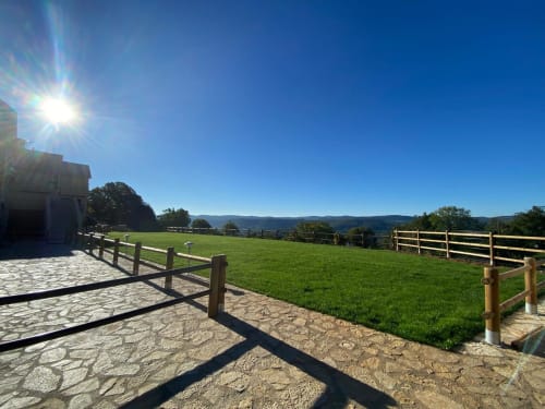 Un jour ensoleillé au gîte Le Domaine du Bez avec ses pâturages verts, clôtures en bois et vue sur les montagnes à Saint Laurent d'Olt