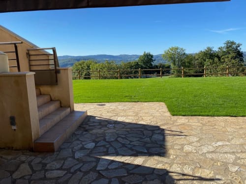La terrasse du gîte Domaine du Bez avec vue sur les montagnes, champs verdoyants et patio en pierre rustique à Saint Laurent d'Olt