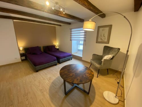 Chambre moderne du Domaine du Bez avec deux lits violets, lampadaire arc, table ronde et fauteuil vert à Saint Laurent