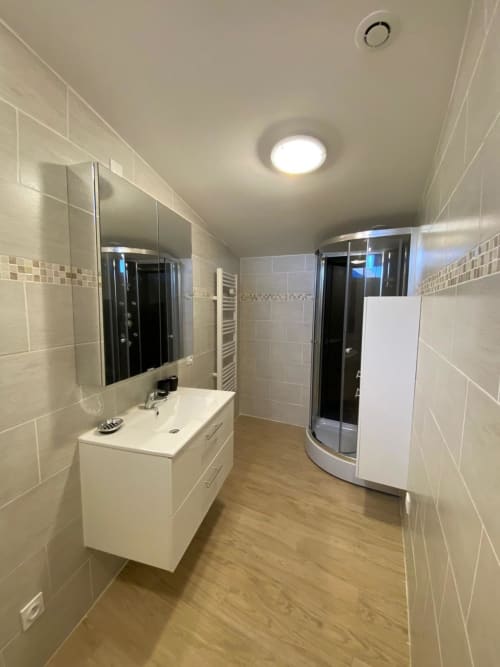 Salle de bain moderne du gîte Le Domaine du Bez avec vasque blanche, grand miroir et douche arrondie à Saint Laurent