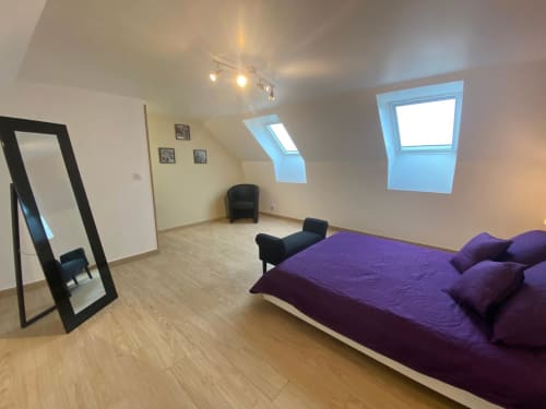 Chambre mansardée moderne au gîte Le Domaine du Bez avec literie violette, fenêtres de toit et parquet.
