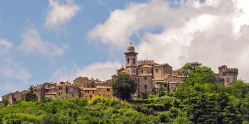 Il borgo medievale di Bracciano arroccato sulla collina: edifici in pietra, torre e rigogliosa vegetazione sotto il cielo azzurro