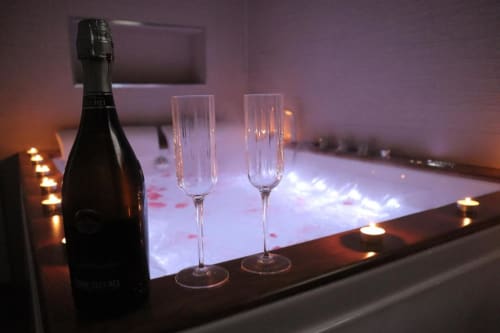 Atmosfera romantica alla Enjoy House Bracciano con champagne, flute, candele e petali di rosa accanto alla vasca illuminata