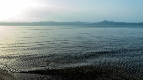 Vista serena del Lago di Bracciano con montagne lontane sotto cielo azzurro presso Enjoy House Bracciano