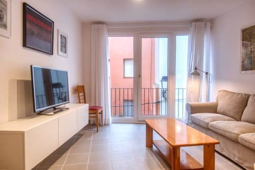 Bright renovated apartment living room in Palafrugell with TV, wooden table, beige sofa, and balcony overlooking the coast