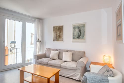 Bright living room in Palafrugell apartment with gray sofa, wooden table, balcony doors, and coastal views.