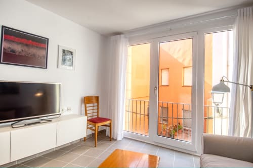Modern apartment living room in Palafrugell with TV, balcony doors overlooking orange building, comfortable seating, and