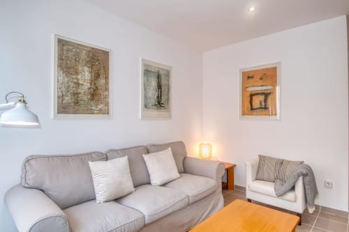 Modern living room in Palafrugell apartment with gray sofa, armchair, framed artwork, and orange accent rug