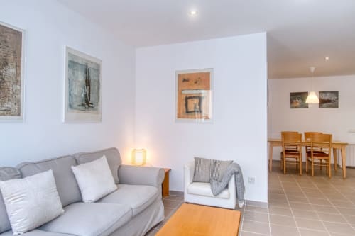 Modern living room in renovated Palafrugell apartment with gray sofa, artwork, dining area, and contemporary furnishings