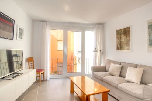 Modern living room in Palafrugell apartment with sofa, wooden table, TV, and balcony doors opening to orange railings