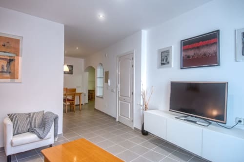 Modern living room in Palafrugell apartment with TV, armchair, wood table, and hallway entrance