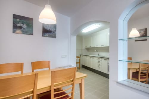 Modern dining area with wooden table and chairs, pendant lighting, and open kitchen with white cabinets in Palafrugell