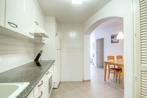 Modern galley kitchen with white cabinetry, gray granite counters, and archway to dining area in renovated Palafrugell