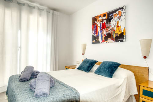 Bright bedroom in Palafrugell apartment with two beds, teal pillows, wooden furniture, and coastal wall art