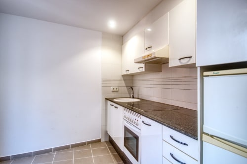Modern white kitchen with dark countertop, oven, and sink in beachfront studio apartment near Palafrugell