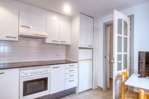 Modern white kitchen with oven, stovetop, and dining area in beachfront studio apartment, Palafrugell