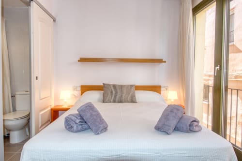 Bright beach apartment bedroom in Palafrugell with wooden bed, rolled towels, and sea view balcony access