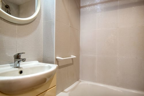 Modern bathroom with white sink, tiled walls, mirror, and bathtub in beachfront apartment Palafrugell