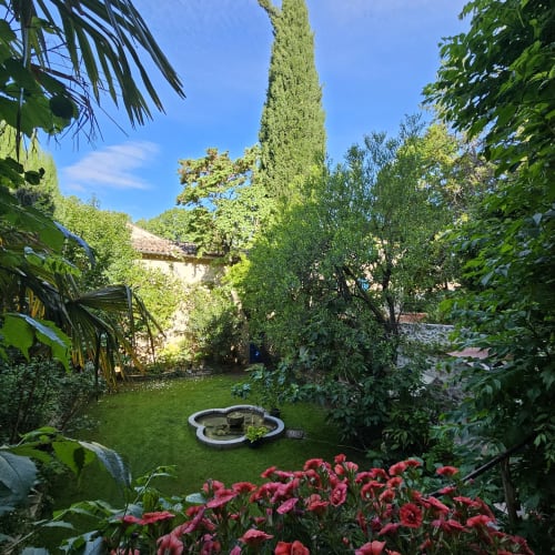Jardin luxuriant de la Cordeline B&B à Brignoles avec bassin circulaire, fleurs rouges et bâtiment en pierre couvert de lierre