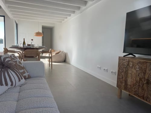 Sala de estar de villa moderna com vista para o mar, sofá cinzento, mesa de jantar em madeira, TV em móvel esculpido e ambiente luminoso