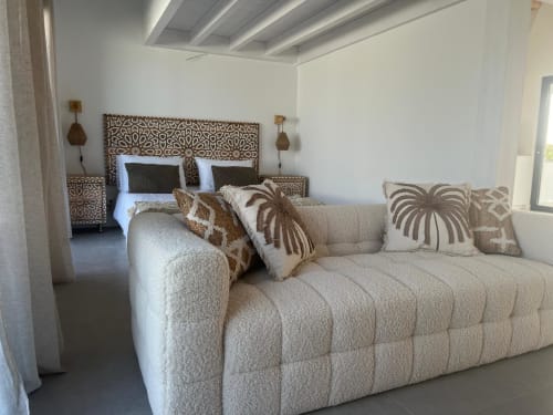 Ampla sala de estar de villa com sofá creme, almofadas decorativas, cama com cabeceira de padrão madeira e teto moderno