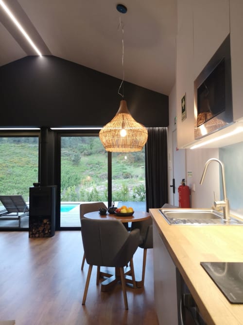 Cozinha e sala de jantar modernas com luminária de fibra tecida, vista para as montanhas através de janelões na villa Em Xisto