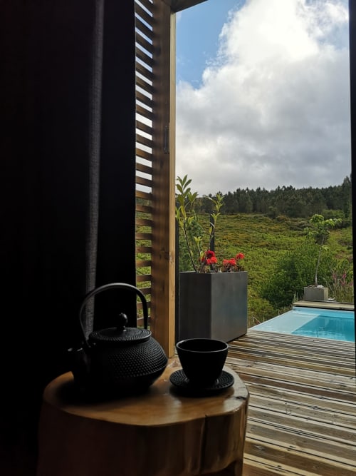 Bule e xícara pretos sobre mesa de madeira com vista para piscina e montanhas na Vila Em Xisto, Góis