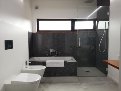 Banheiro moderno com paredes de mármore negro, louças brancas, banheira, duche de walk-in, bidé na villa Em Xisto na serra de Góis